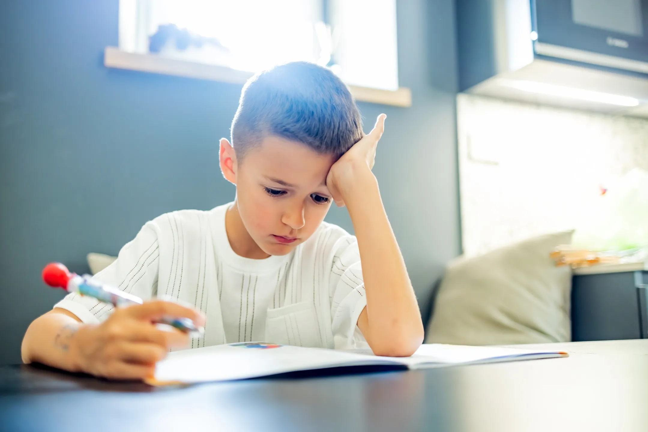 Schuljunge wirkt frustriert bei den Hausaufgaben und haelt einen Stift